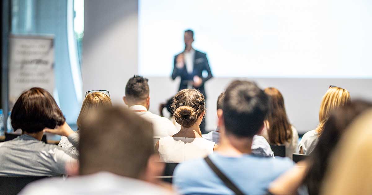 Male speaker giving a talk in conference hall at business event. Audience at the conference hall. Business and Entrepreneurship concept. Focus on unrecognizable people in audience.